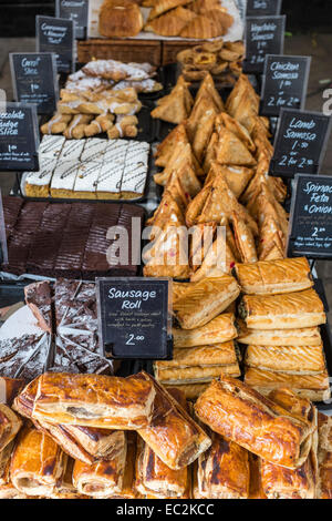 Wurstbrötchen und andere Häppchen und Kuchen zum Verkauf auf einem Marktstand. Stockfoto