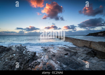 Dramatischen Sonnenuntergang und Wellen an der Pier in Porthleven Hafen an der Küste von Cornwall in der Nähe von Helston Stockfoto