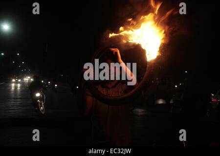 Lahore. 8. Dezember 2014. Eine pakistanische Aktivist aus Pakistan Tehreek-e-Insaaf (PTI) Oppositionspartei hält einen brennenden Reifen bei einem Protest gegen die Tötung der einen Partei-Arbeiter in Lahore, 8. Dezember 2014. Mindestens ein PTI Arbeiter starben und 11 Personen, darunter zwei Polizeibeamte bei Auseinandersetzungen zwischen Arbeitern der PTI und Pakistan Muslim League-Nawaz in Faisalabad am Montag verletzt. © Jamil Ahmed/Xinhua/Alamy Live-Nachrichten Stockfoto