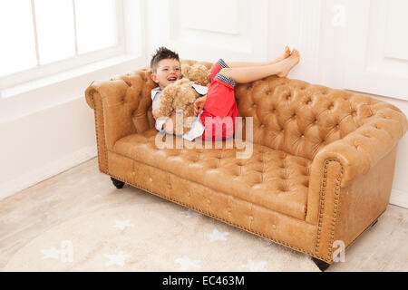 Kleiner Junge hält Spielzeug und Lachen zu Hause auf Sofa liegend Stockfoto