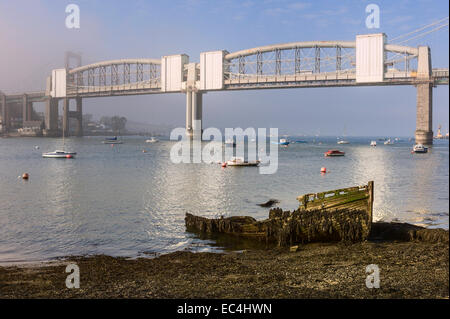 Ein verfallenes Holzboot liegt am Ufer des Flusses Tamar mit wunderschönen Royal Albert Bridge als Kulisse im Morgengrauen verstoßen, Stockfoto