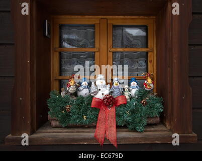 Verschiedene Weihnachtsfiguren, die am Fenster eine Holzhütte im freien Stockfoto