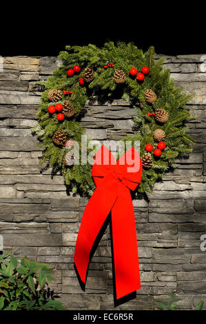 Weihnachten Kranz mit Tannenzapfen und großen roten Bogen hängen auf einer Natursteinmauer Stockfoto