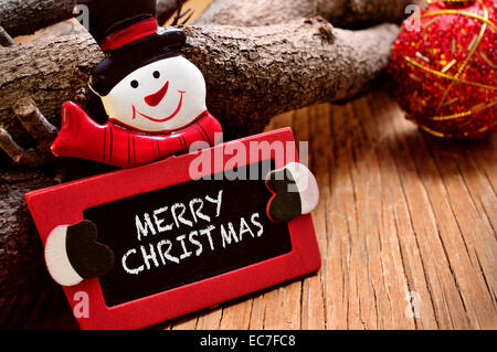 der Satz Frohe Weihnachten, geschrieben in einer Tafel in der Form eines Schneemannes auf einer rustikalen Holzoberfläche Stockfoto