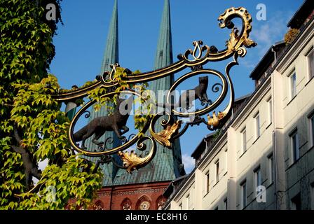 BERLIN, Deutschland: Vergoldeten schmiedeeisernen Ladenschild im Nikolaiviertel mit zwei Türme von der Nikolaikirche im Hintergrund Stockfoto