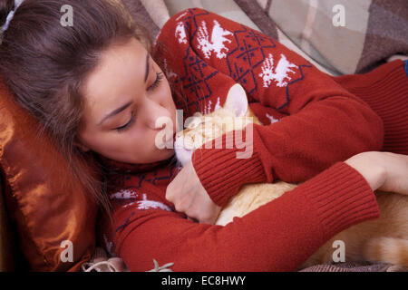 Niedliche Mädchen küsst eine rote Katze auf der Nase Stockfoto