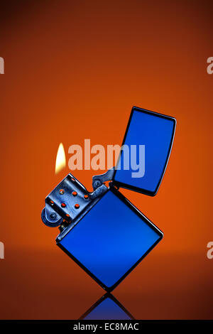 Blaue Zippo-Feuerzeug mit Flamme auf orangem Hintergrund Stockfoto