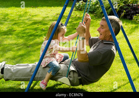 Großvater und Enkelin auf Schaukel im Garten sitzen. England, UK. September Stockfoto