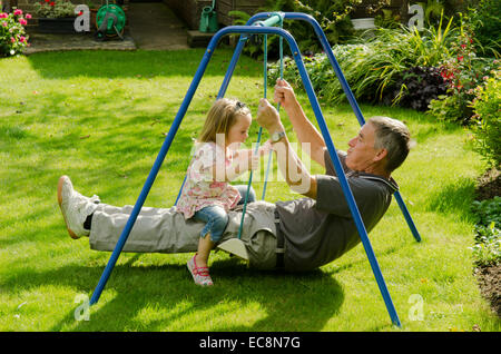 Großvater und Enkelin auf Schaukel im Garten sitzen. England, UK. September Stockfoto