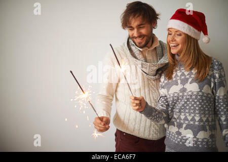 Glückliche junge Mann und ein Mädchen in Santa Cap Bengal-Lichter in ihren Händen zu betrachten Stockfoto