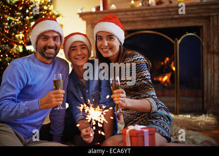 Mann und Frau in Santa Caps mit ihrem Sohn Holding Bengal Licht zwischen ihnen Toasten Stockfoto