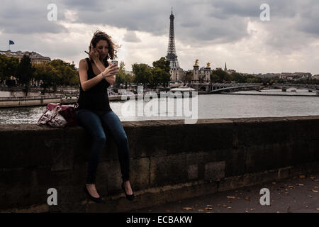 Schwangere Frau allein in Paris bereitet sich auf eine Selfie an einem windigen Tag zu nehmen. Im Hintergrund ist der Eiffelturm. Stockfoto