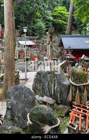 Shinto-Friedhof am Schrein von Fushimi Inari-taisha, Kyoto, Japan, mit magischen Kitsune (Füchse) und Opfergaben von roten Torii-Miniaturtoren Stockfoto