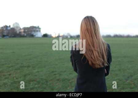 Hintere Ansicht Schuss eine junge Frau steht auf der Suche in die Ferne in einem Park. Stockfoto