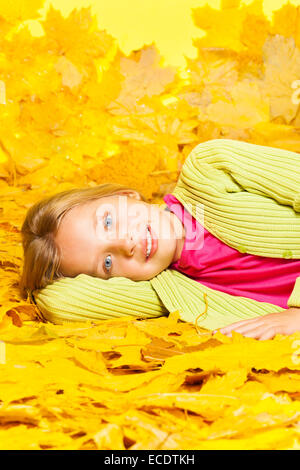 Kleines blondes Mädchen legt auf das gelbe Herbstlaub Stockfoto