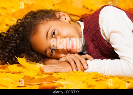 Afrikanische Mädchen legt auf gelbes Herbstlaub Stockfoto