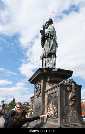 Zwei Touristen berühren und reiben Sie die Oberfläche einer Statue auf der Karlsbrücke als Glücksbringer, Prag, Tschechien Stockfoto