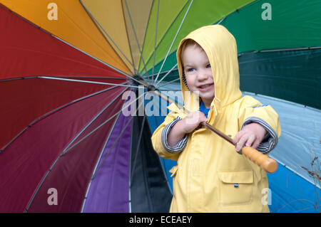 Junge in einem Regenmantel mit mehrfarbigen Regenschirm Stockfoto