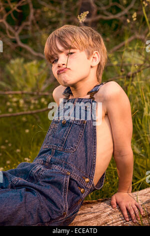 Bildnis eines Knaben sitzen auf einem Baumstamm lustige Grimassen Stockfoto