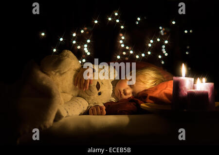 Kerzen neben einem schlafenden Jungen, der einen Teddybären kuschelt Stockfoto