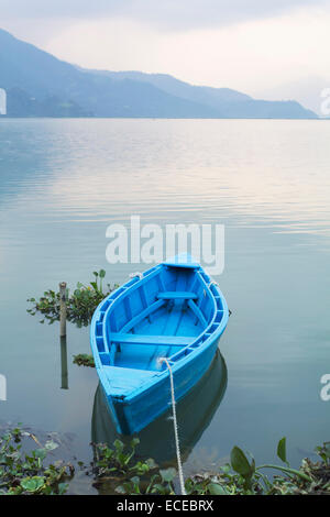 Nepal, Western Region, Gandaki Zone, Pokhara, Mansawar, Phewa See, blaue Ruderboot in See mit Silhouette des Berges im Hintergrund verankert Stockfoto