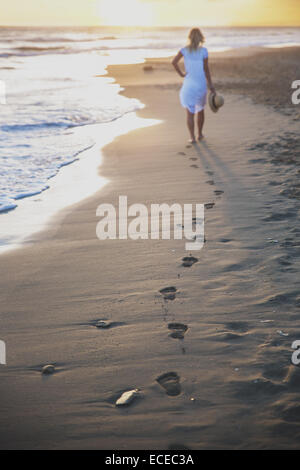 Schöne Frau am Strand mit ihren Fußspuren zurück Stockfoto