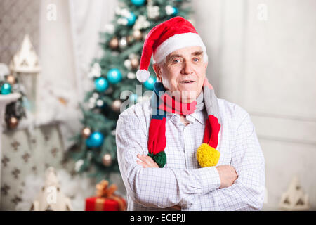 Porträt von reifer Mann in Hut und hellen Schal stehend mit Armen Weihnachtsmann gekreuzt über Weihnachten Hintergrund Stockfoto