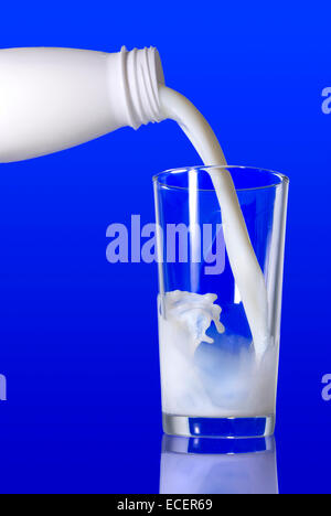 Milch aus der Flasche in Glas gießen, auf blauem Hintergrund Stockfoto