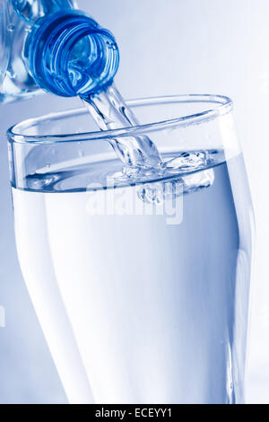 Gießt Wasser aus der Flasche ins Glas in blauen Tönen Stockfoto