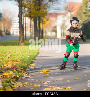 Glückliche kleine Junge im sonnigen Tag auf Rollschuhen Stockfoto