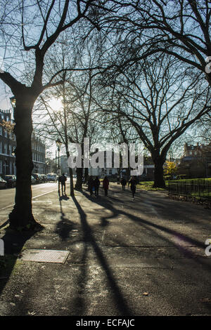 Passanten an einem sonnigen Wintertag in einem Park in Highbury, London, UK mit viel Schatten. Stockfoto