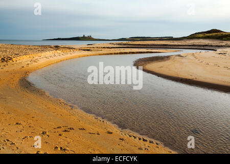 Ein Fluss in die Nordsee bei Newton Links, Northumberland, UK mit Dunstanburgh Castle im Hintergrund. Stockfoto