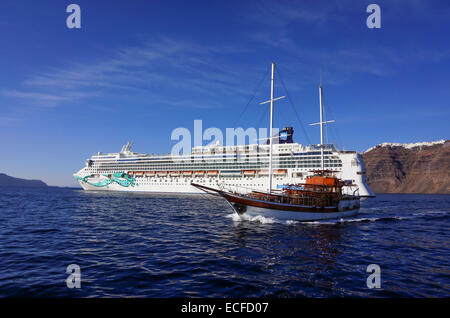 Touristische Yacht vorbei Kreuzfahrtschiff Norwegian Jade unter Klippen und weißen Häusern, Santorini, Griechenland Stockfoto