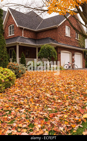 Ahorn-Blätter, die auf einer Wiese vor einem Haus mit dem Fahrrad gefallen sind gegen eine weiße Garage geparkt. Stockfoto