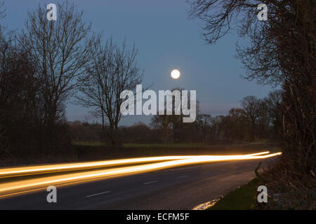 Ein Auto auf einer Landstraße mit einem Vollmond in der Nähe von Preston, Lancashire, UK. Stockfoto