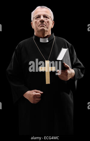Ältere männliche Priester hält eine Heilige Schrift auf schwarzem Hintergrund Stockfoto