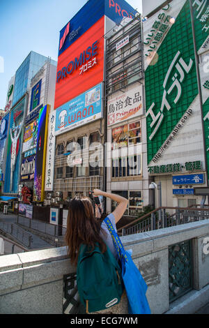 Eine Mädchen nimmt Touristen Bilder auf einer Brücke in Dotonbori, Osaka Stockfoto