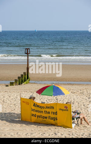 Ein Windschutz RNLI Rettungsschwimmer am Strand von Poole, Dorset, Großbritannien warnt Schwimmer immer schwimmen zwischen den roten und gelben Flaggen Stockfoto