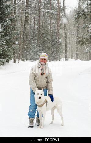 Frau mit einem Hund auf einem Spaziergang in den Wäldern während eines Schneefalls Stockfoto