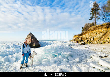 Frau mit Hund spazieren gehen an einem sonnigen Wintertag auf der Küste des Meeres Stockfoto