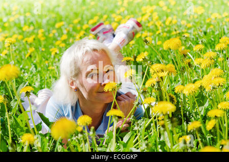 Eine Frau liegt auf einer Lichtung zwischen den Löwenzahn und schnüffelt eine Blume Stockfoto