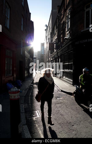 Frau im Sonnenschein und im Schatten zu Fuß an der Ecke von Sandys Zeile & Widegate Street Spitalfields London, UK KATHY DEWITT Stockfoto