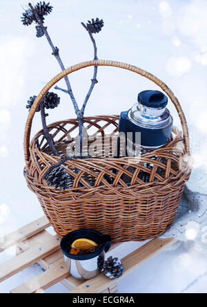 Korb mit Thermoskanne mit Glühwein und gestrickte Decke auf Schlitten im Schnee Stockfoto