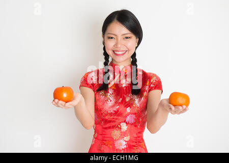 Porträt des chinesischen Asiatin Hände halten Mandarine Frucht, im traditionellen roten Qipao stehen auf einfarbigen Hintergrund. Stockfoto