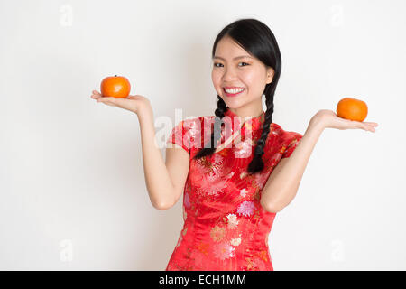 Porträt des chinesischen Asiatin Hände halten Mandarine orange, im traditionellen roten Qipao stehen auf einfarbigen Hintergrund. Stockfoto