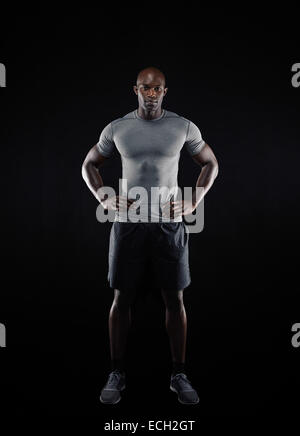 In voller Länge Portrait von muskulösen jungen Mann in Sportbekleidung Blick in die Kamera vor schwarzem Hintergrund. Starken afrikanischen Sportler. Stockfoto