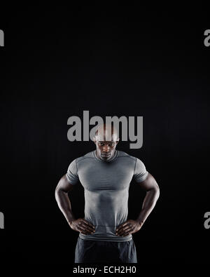 Porträt von muskulösen jungen Mann in Sportbekleidung starrte auf Kamera auf schwarzem Hintergrund. Afrikanische Sportler mit seinen Händen auf den Hüften Stockfoto