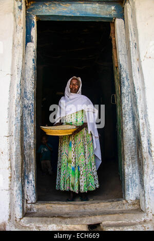 Freundlichen alten Frau mit einem Korb von Mais in einen Türrahmen in der Nähe von Keren, Eritrea Stockfoto