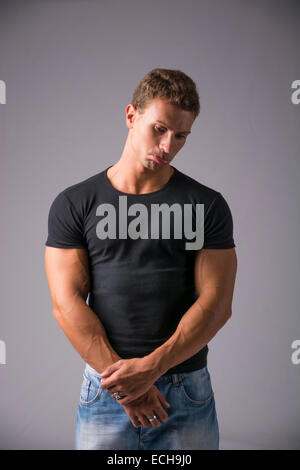Schön bemuskelt Jüngling in schlichtes schwarzes Hemd und blaue Jeans Blick in die Kamera in traurigen Gesichtsausdruck mit Pouting hautnah Stockfoto