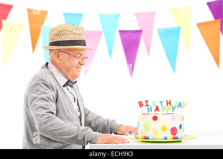 Glücklich Senior sitzt an einem Tisch mit Geburtstagstorte isoliert auf weißem Hintergrund Stockfoto